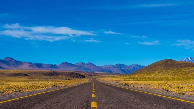 Empty open highway stretching toward mountains under a clear blue sky