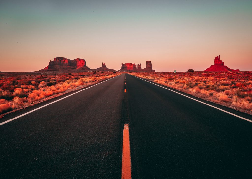 Open desert highway stretching toward Monument Valley rock formations at sunset