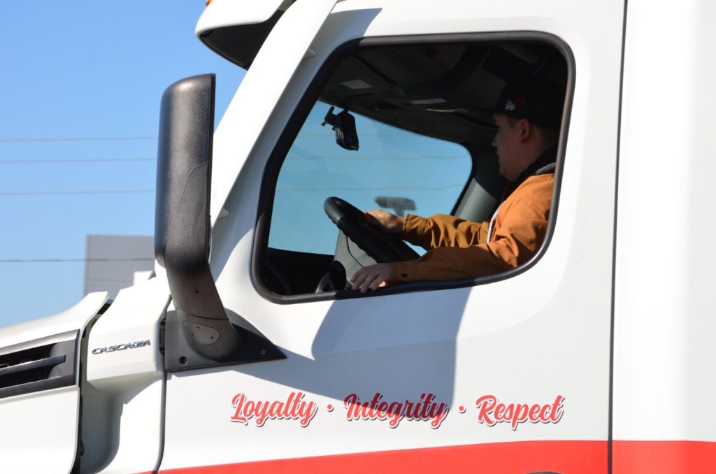 CDL student driver behind the wheel of a Southwest Truck Driver Training semi-truck with 'Loyalty · Integrity · Respect' on the cab