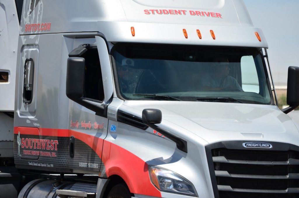 Close-up of a Southwest Truck Driver Training semi-truck cab with student driver and instructor visible through the windshield