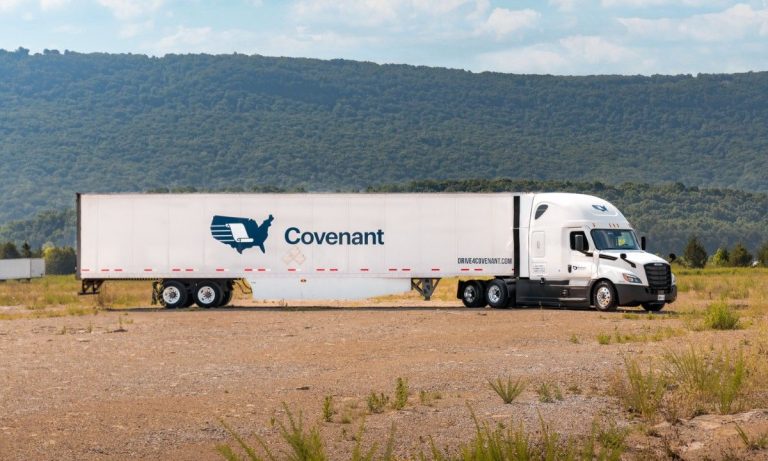 Covenant Transport semi-truck and trailer parked in a rural setting with wooded hills in the background