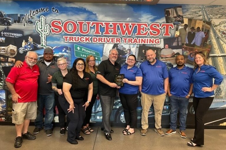 Schneider National representatives presenting a top school award plaque to Southwest Truck Driver Training staff in front of the company's welcome mural