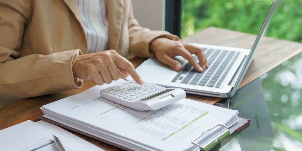 Person using a calculator and laptop to review financial documents for CDL training tuition planning