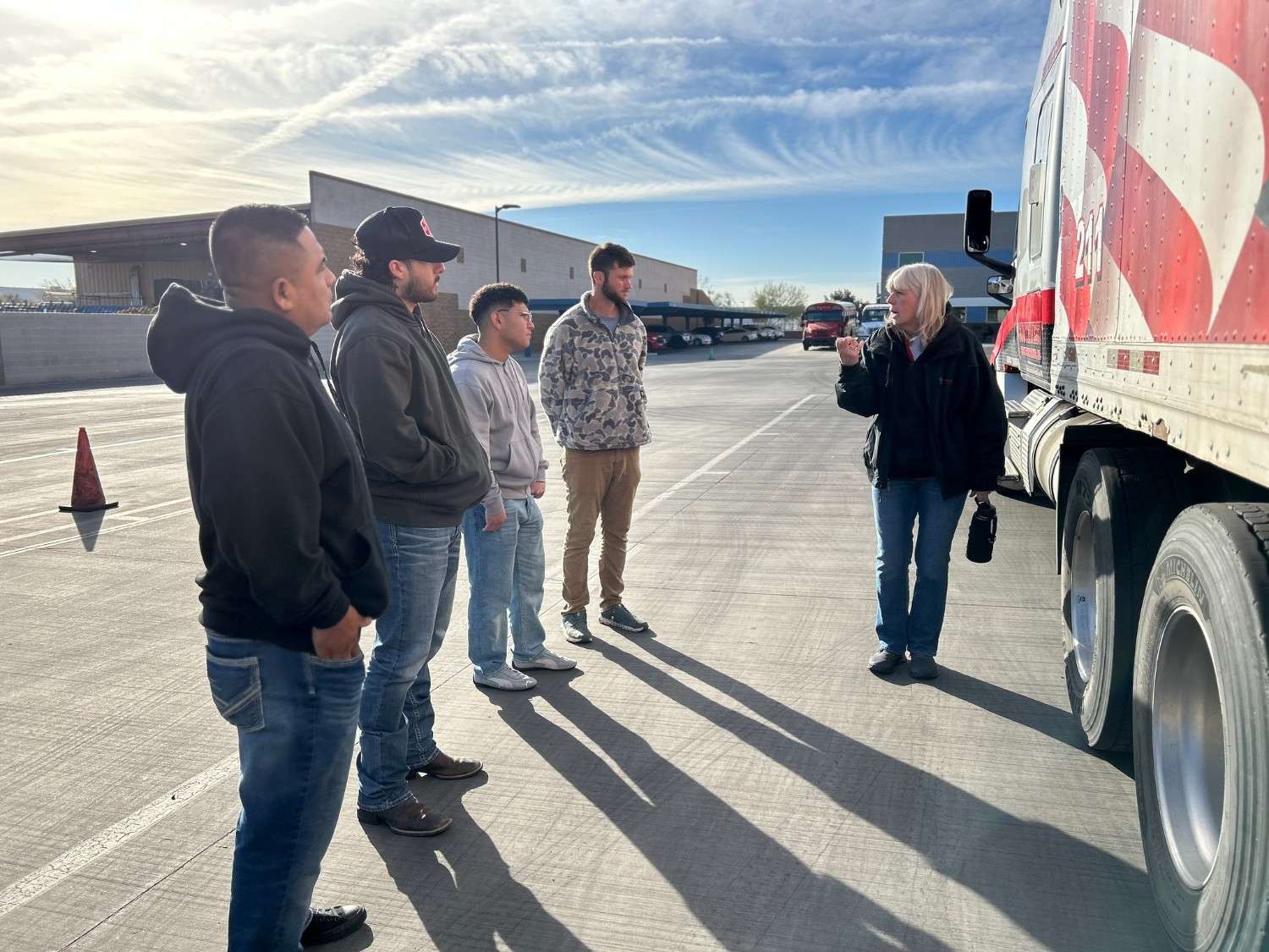 Female CDL instructor teaching a group of truck driving students next to a semi-truck