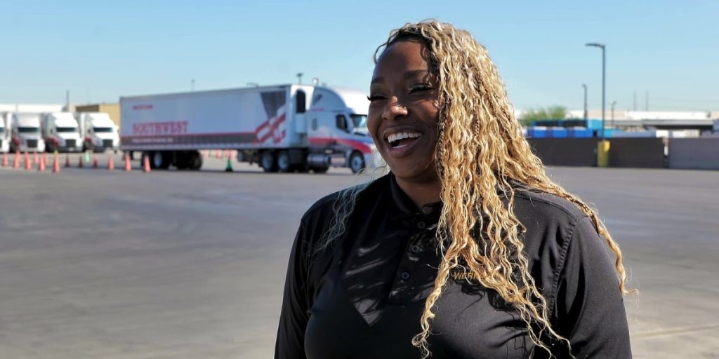Nicole smiling and standing in Southwest Truck Driver Training yard with a semi truck behind her