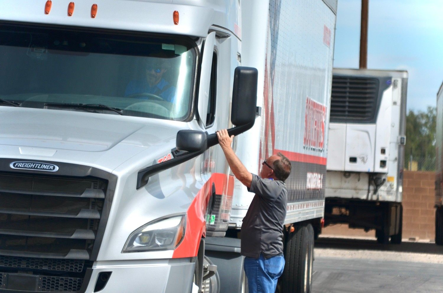CDL instructor signaling a student driver in a semi-truck during behind-the-wheel training