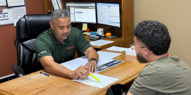 An admissions representative in a green Southwest Truck Driver Training polo uses a highlighter to point to details on enrollment paperwork while meeting with a prospective student across his desk.