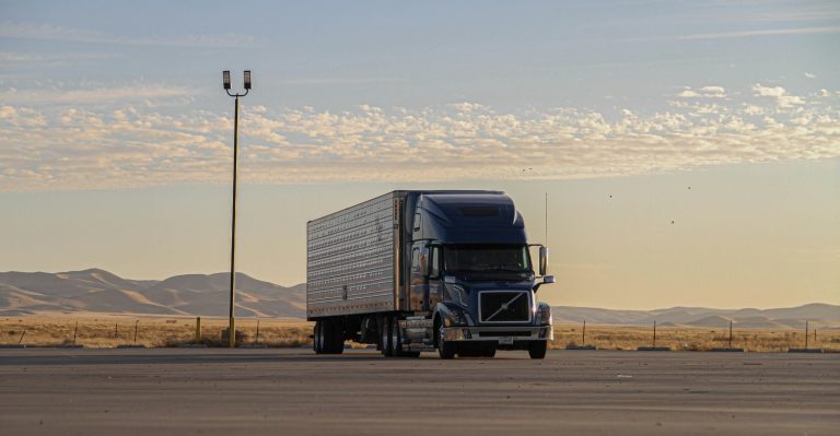 Semi truck sitting in a parking lot in front of rolling hills of sand